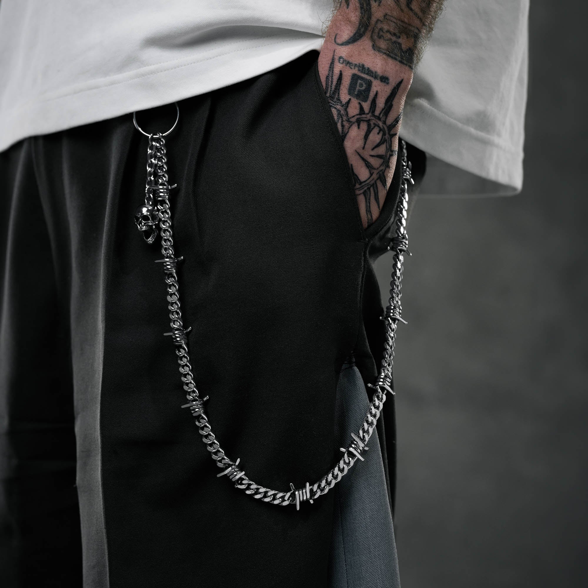 9mm barbed wire cuban wallet chain featuring skull charm on cable link chain on body beside pocket grey pants