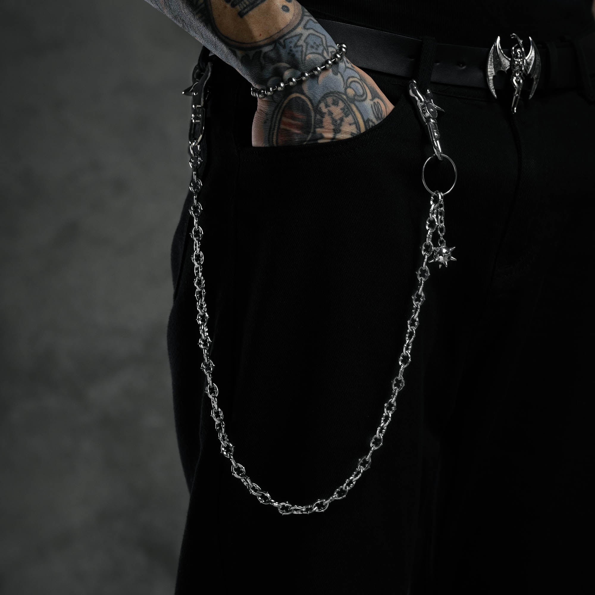 9mm spiked cable link wallet chain featuring spiked ball charm on cable link chain on black pants with tattooed hand in pocket 