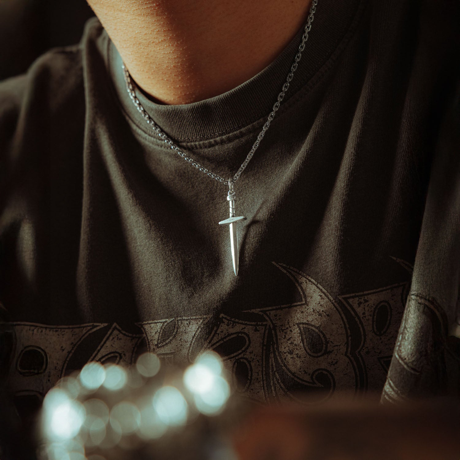 Silver chain with a dagger pendant on it, engraved with "Statement" on male model 