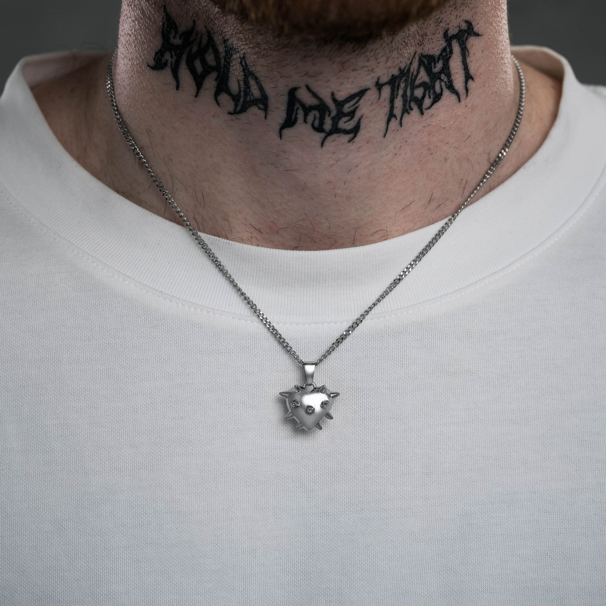 Silver Spiked heart pendant on a curb chain on male model with neck tattoo and white tee