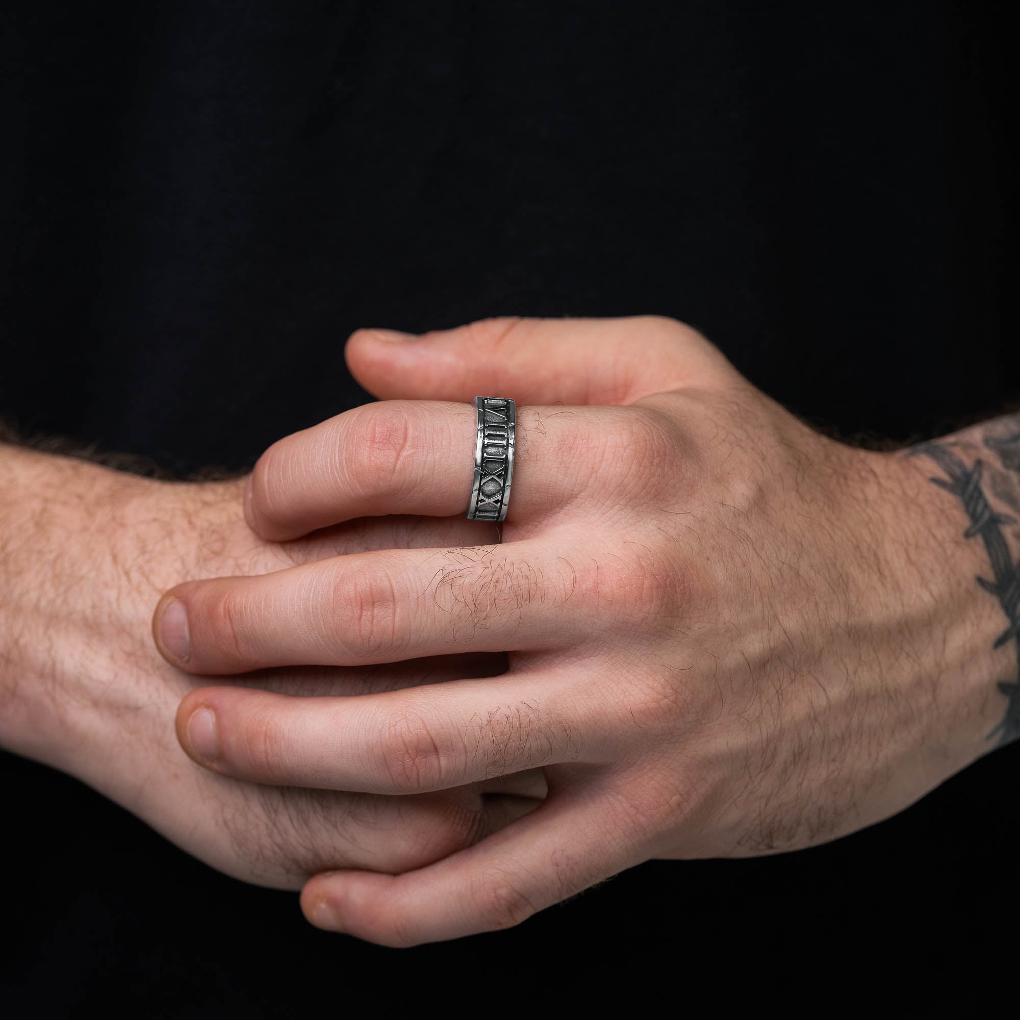 Silver band ring with roman numerals embedded around entirety of ring band. on male model