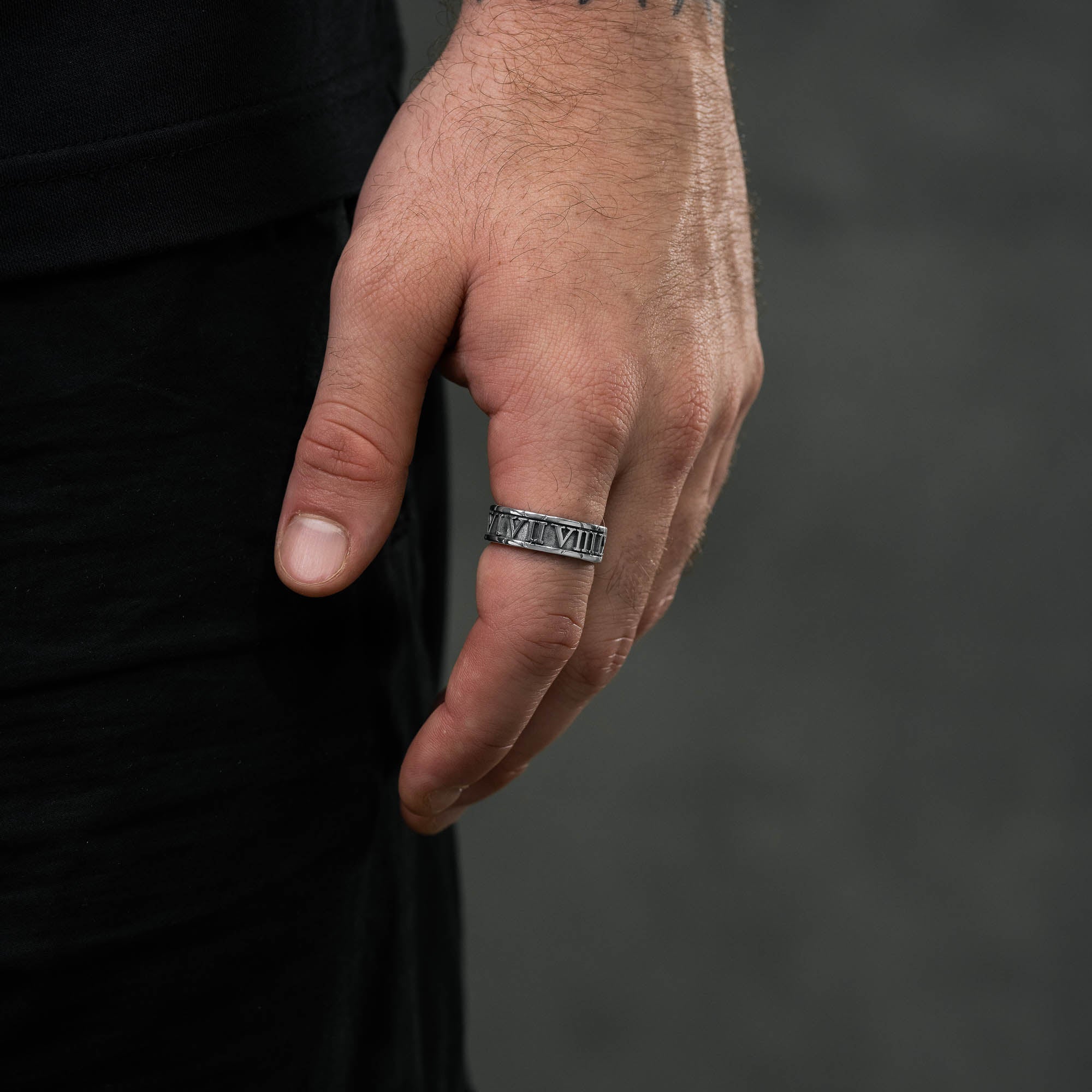 Silver band ring with roman numerals embedded around entirety of ring band. on male model