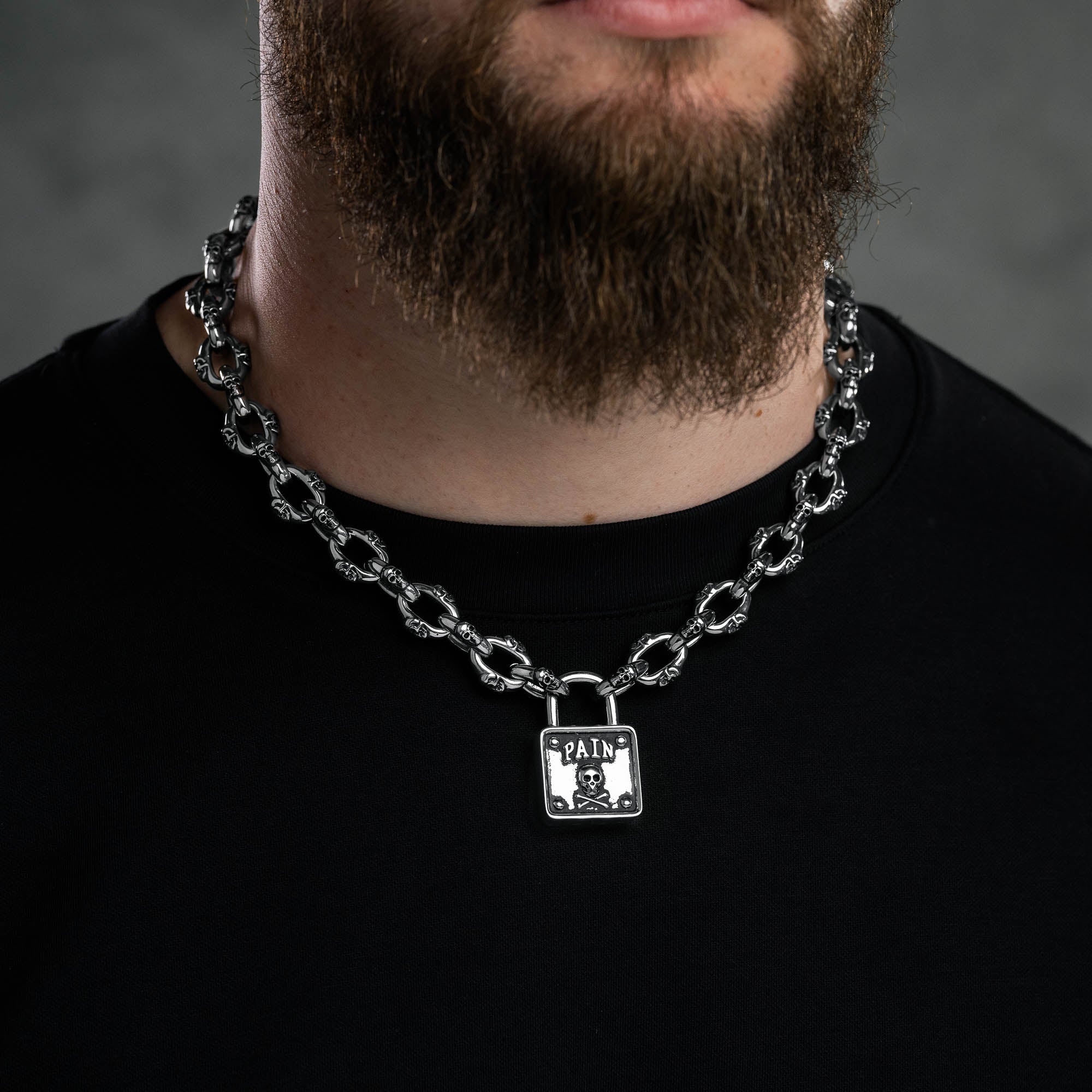 Silver skull chain with padlock pendant with skull and word "pain" embedded above skull, on male model 