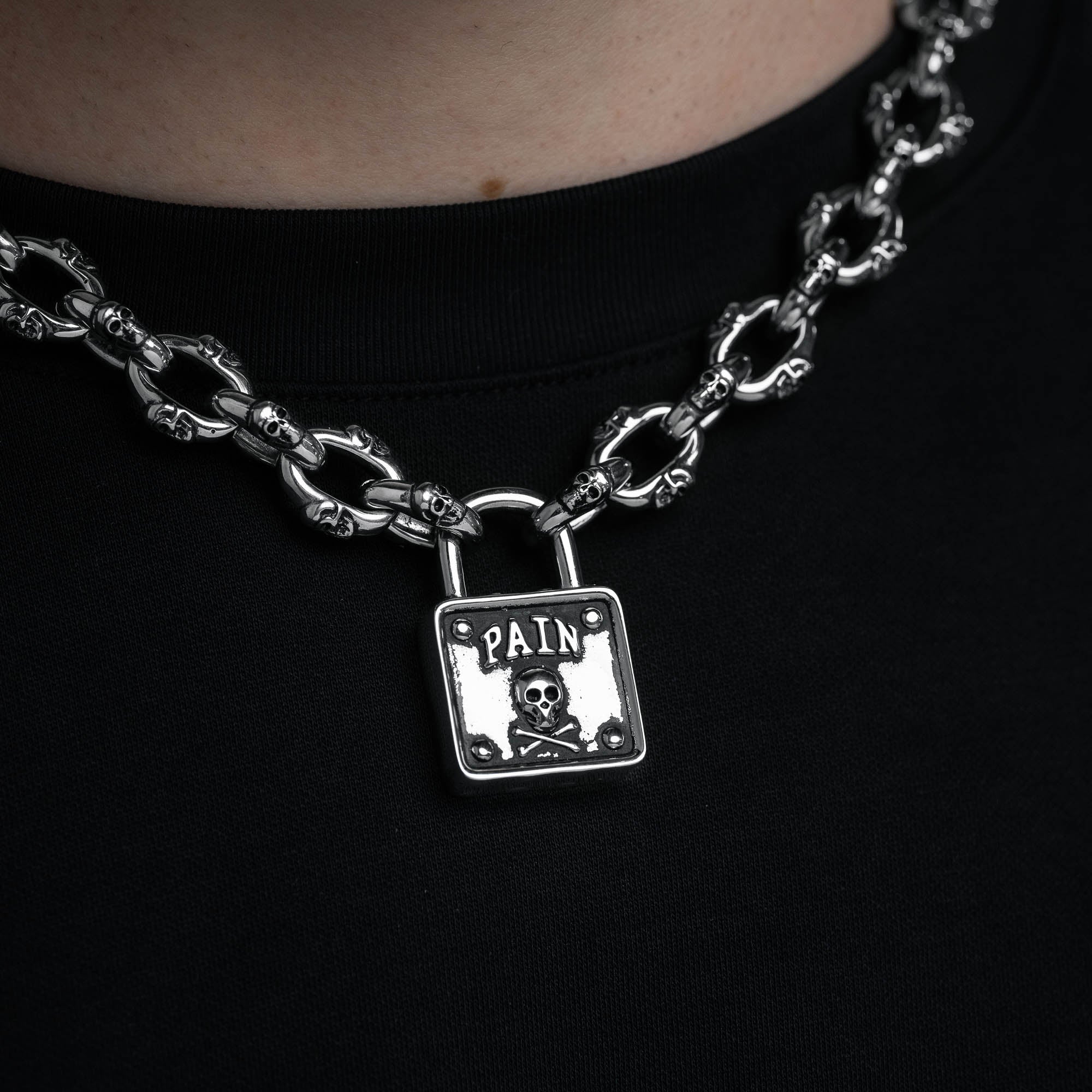 Silver skull chain with padlock pendant with skull and word "pain" embedded above skull, on male model 